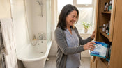 A woman taking incontinence pads from the cupboard in her bathroom