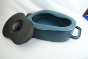 a bed pan with lid placed on a bed with the lid just to the side.