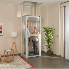 Two people inside a Stannah S2 home lift in a living room setting.